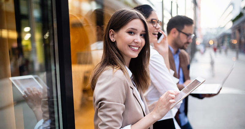 Woman smiling as she stands in front of city building using device